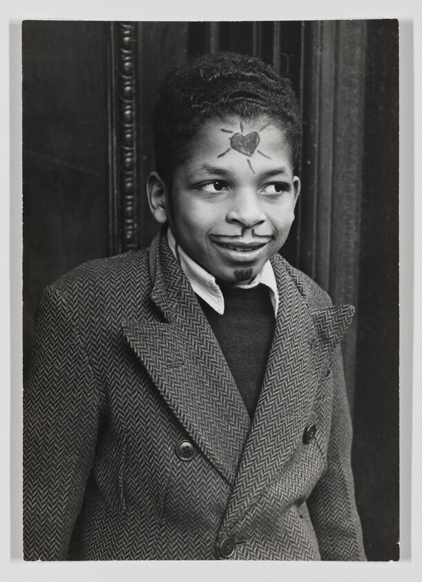 Young boy with a drawn heart on his forehead and marker face markings wearing a coat.