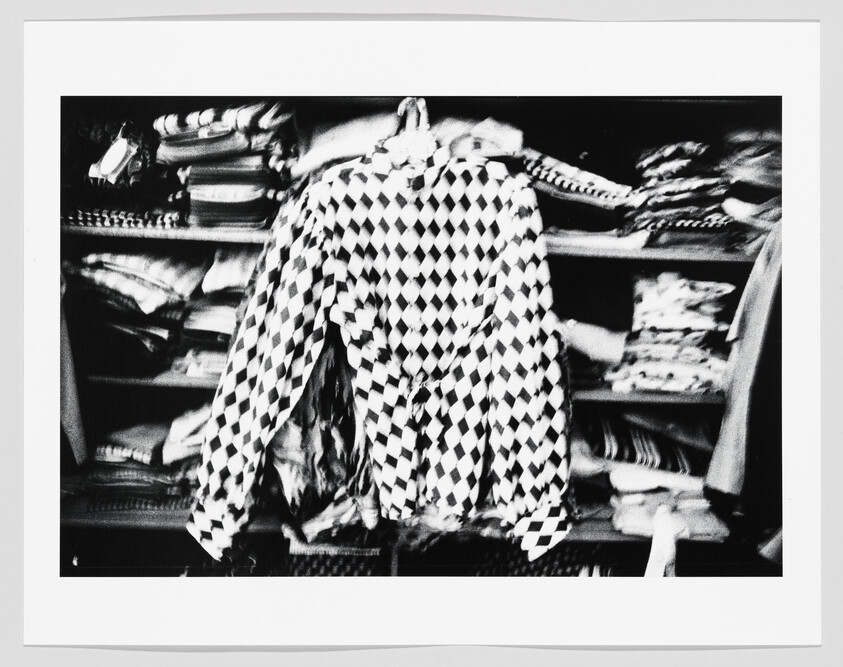 A black-and-white diamond-patterned jacket hangs on a hanger in front of folded clothing shelves.