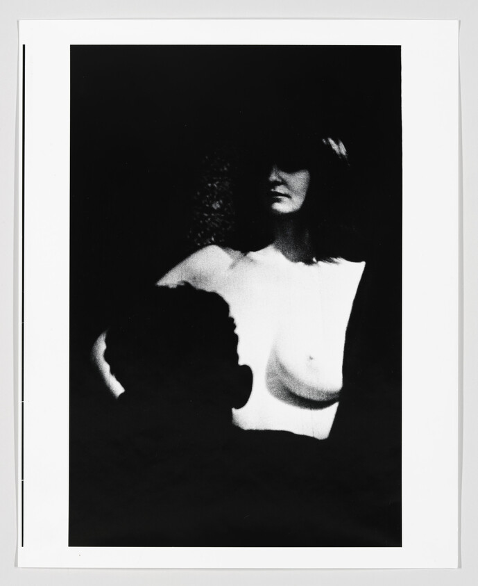 A high-contrast black-and-white portrait of a partially nude woman with a silhouetted figure in the foreground.