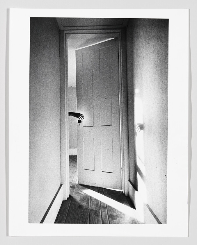 A partially open door with a hand reaching through the doorway and a shadow on the wall.