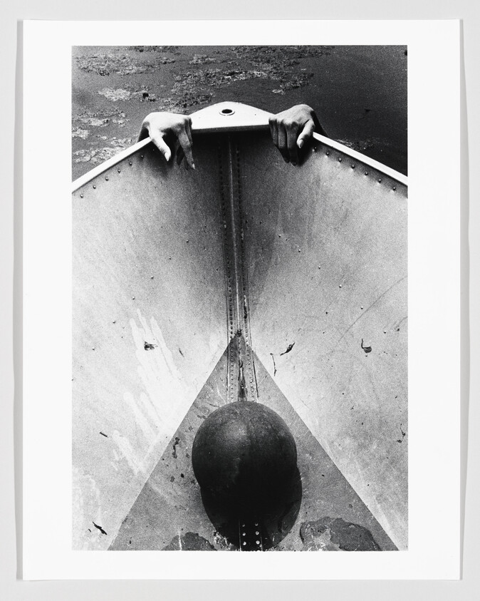 Two hands gripping the front of a metal boat as it floats in dark water.