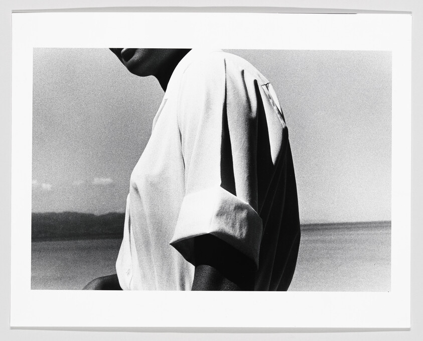 A person wearing a short-sleeve shirt stands by a calm seaside horizon.