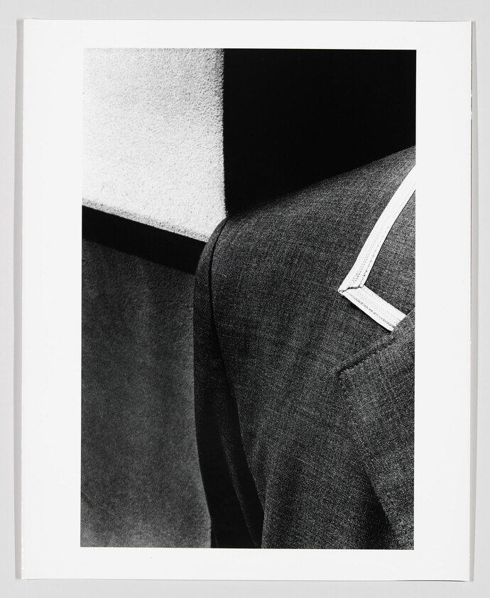 Close-up of a suit jacket shoulder and lapel beside a textured wall, shown in black and white.