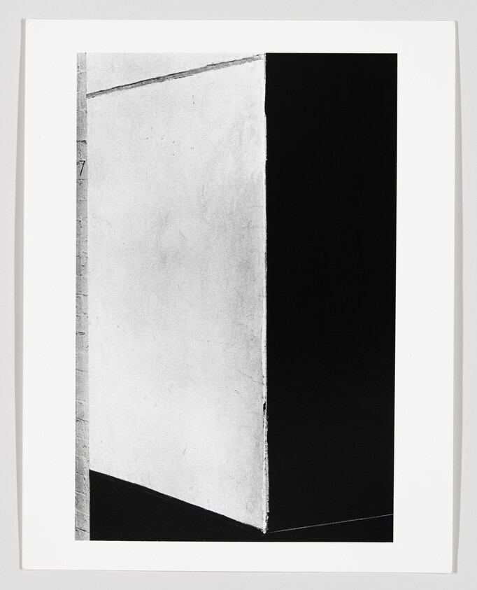 Tall white wall corner casting a triangular shadow against a deep black background.