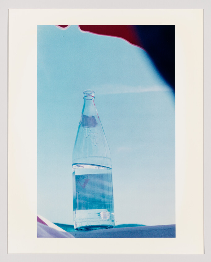 A clear glass bottle half-filled with water stands against a bright blue sky.