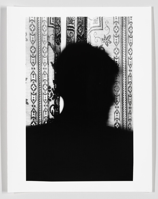 Silhouette of a person's head cast against a patterned curtain with floral and geometric designs.