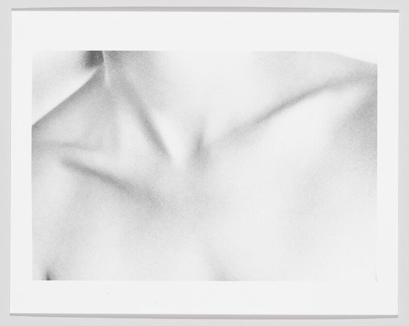A black-and-white close-up of a person's collarbones and upper chest framed on a white mat.