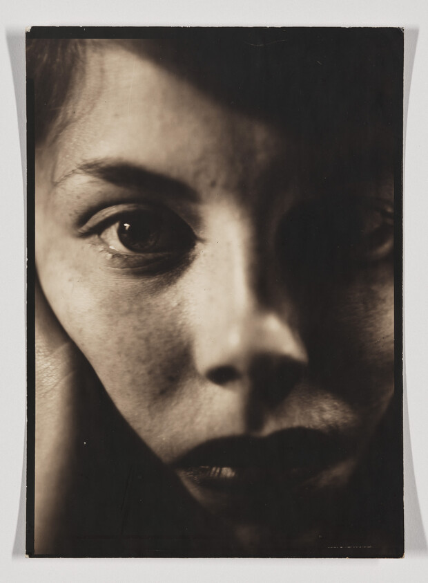 Close-up of a woman's face with an intense gaze and deep shadow across one eye.