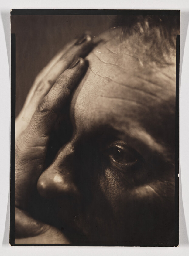 Elderly person pressing a hand to their forehead, staring pensively into the distance.