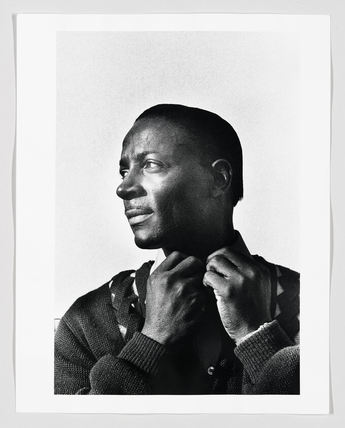 Man adjusts his sweater collar while looking thoughtfully to the left.