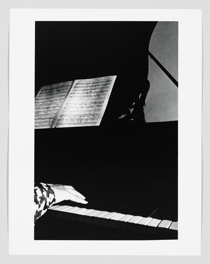 A hand plays piano keys while sheet music is open on the music stand.