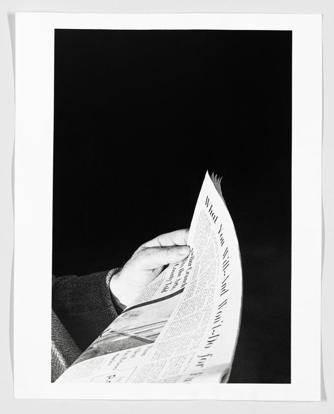 A person’s hand turning a folded newspaper page against a dark background.