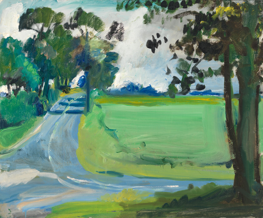 A winding country road curves past trees beside a wide green field under a cloudy sky.