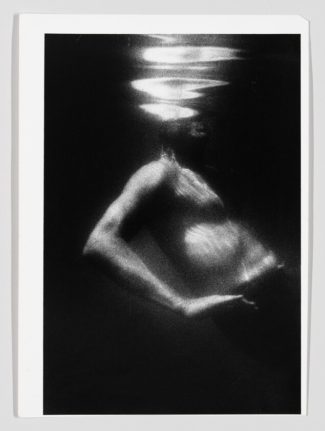 A submerged person with one arm bent and light rippling across their head and torso.