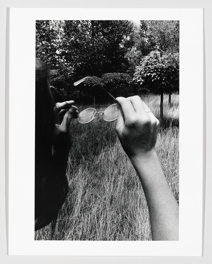 A person holding round eyeglasses up while standing in a tall grassy field.