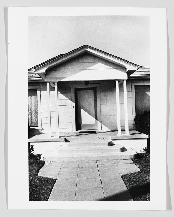 A house front with a small porch, two columns, and concrete steps leading to the door.