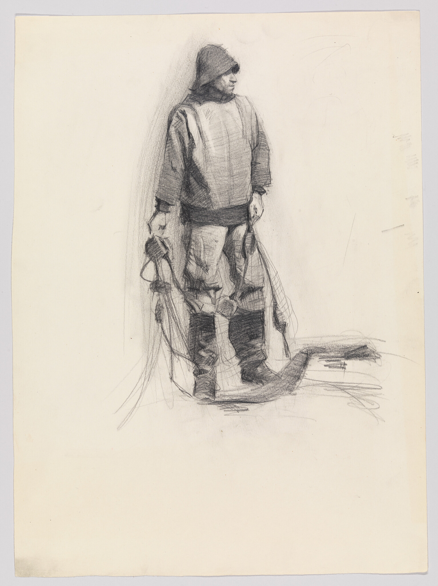A person in a hooded coat and heavy boots stands holding fishing nets and ropes.