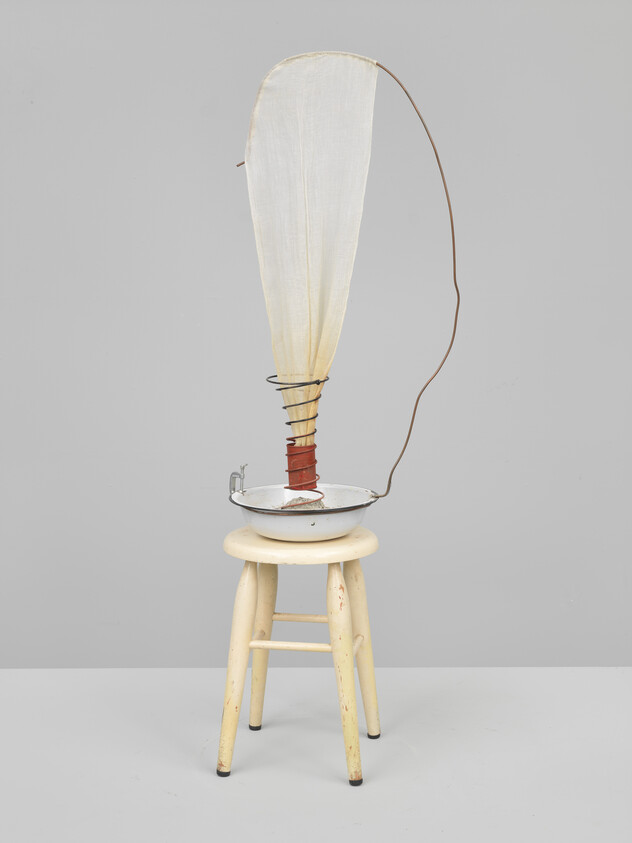 A small wooden stool holds a metal basin with a tall fabric funnel held by wire.