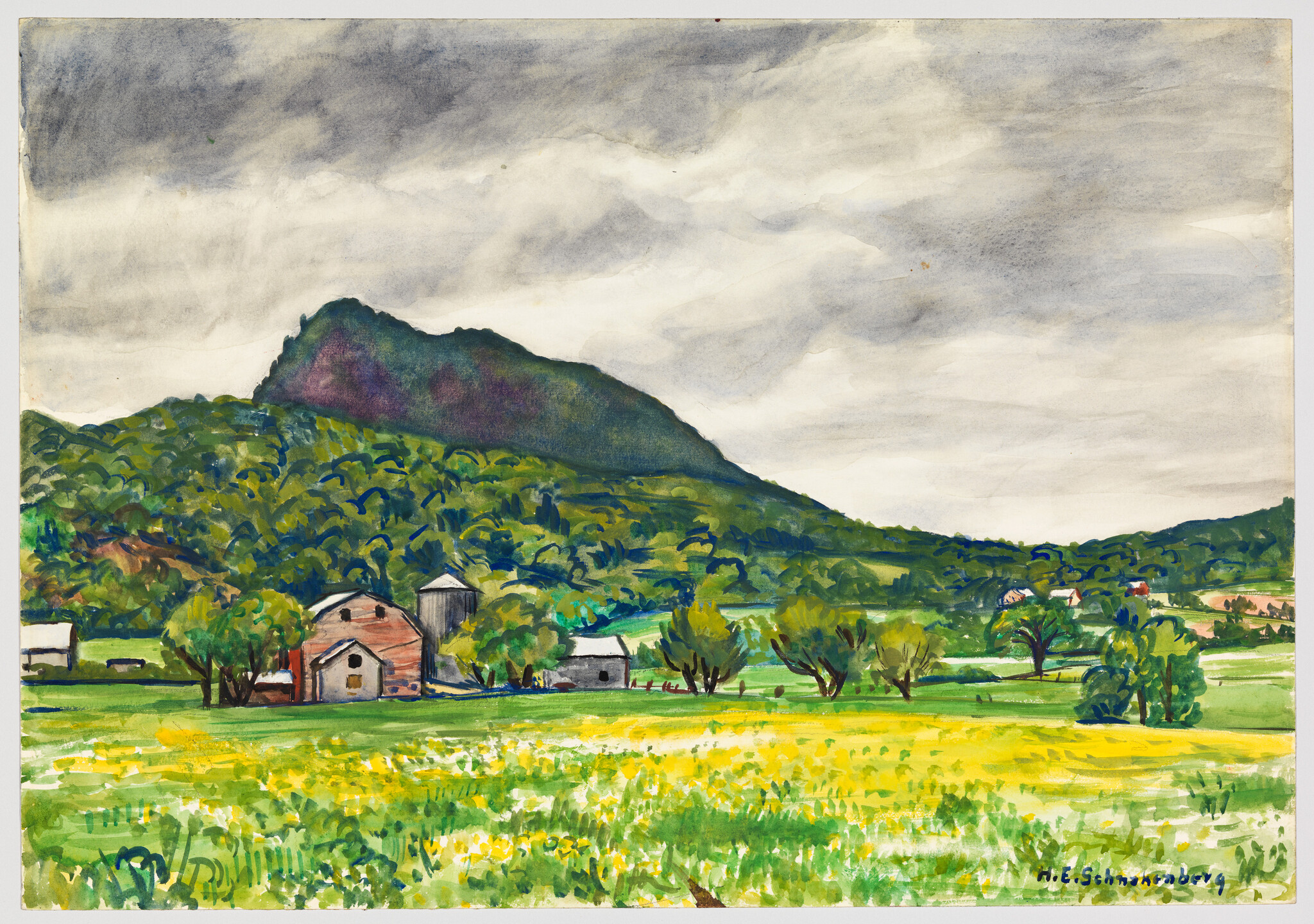 A barn and silo sit in a green field below a forested hill under a cloudy sky.
