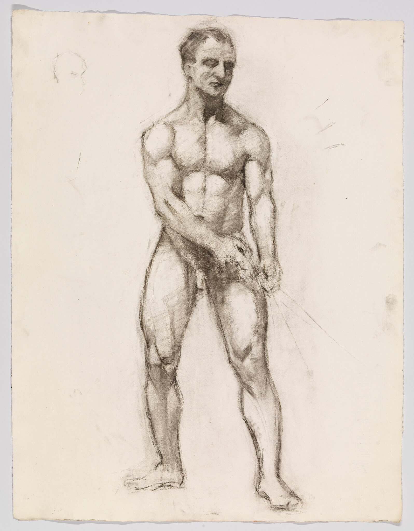 Standing male figure drawn in charcoal with hands held near his groin and strong muscular shading.