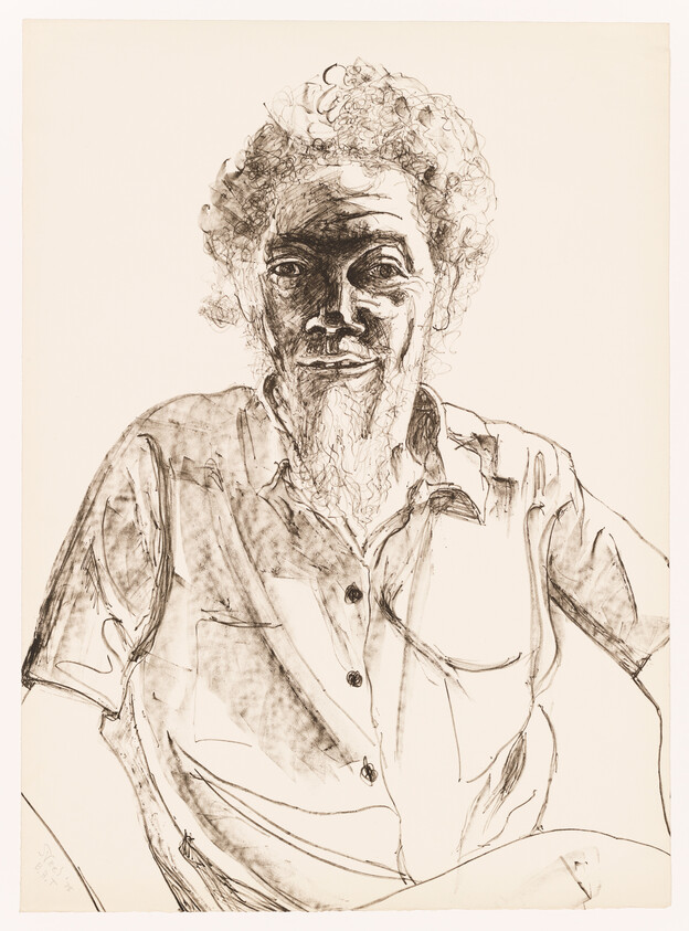 An elderly man with curly hair and a beard sits wearing a button-up shirt.