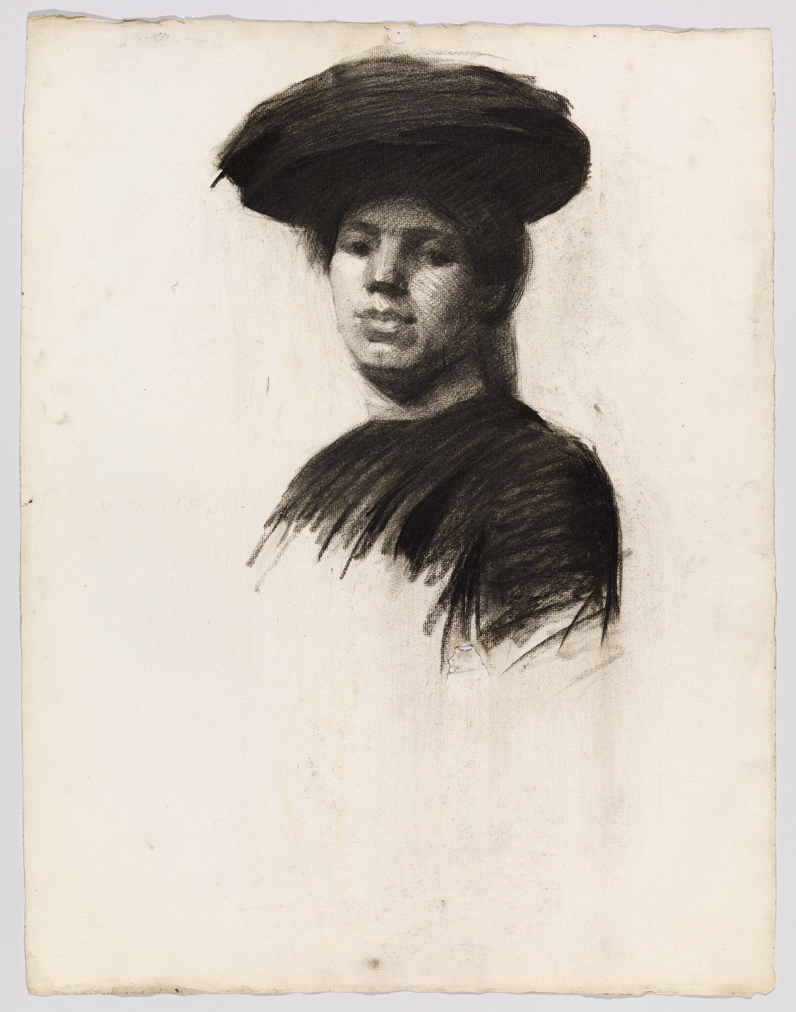 Young person wearing a wide-brim hat and dark clothing looking toward the viewer.