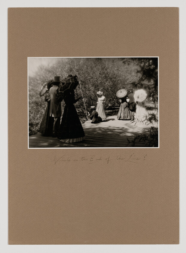 Victorian-era people standing on a wooden walkway, women holding parasols and a child sitting nearby.