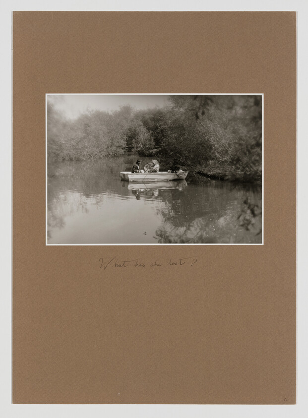 Three people sit in a small rowboat on a calm river surrounded by trees.
