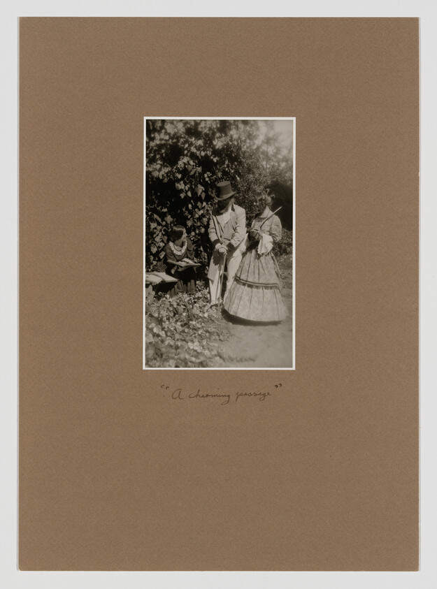 A sepia-toned vintage photograph mounted on a brown paper background, depicting three people in a garden setting. A man in a suit and top hat is seated next to a woman in a full-skirted dress and bonnet, both are looking at a book held by a young boy. The image is captioned with the phrase "A charming passage" in cursive handwriting at the bottom.
