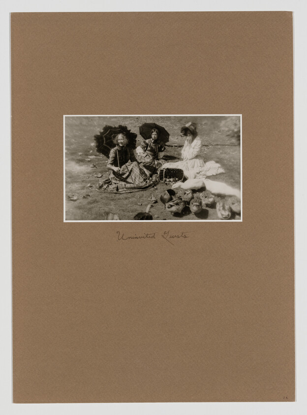 Three girls in old-fashioned dresses sit on the ground with parasols and a basket of items.