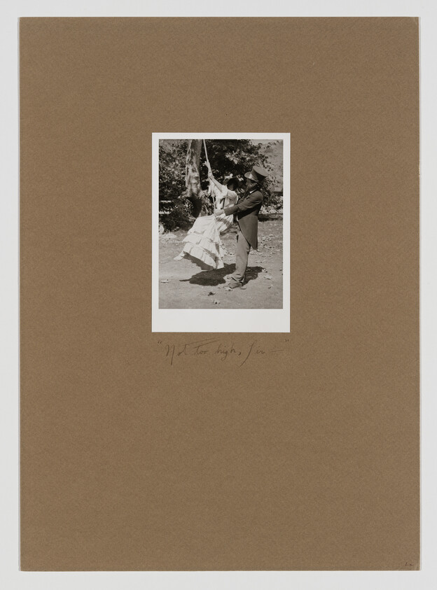 A vintage black and white photograph mounted on a brown paper background. The photo depicts a person in a long dress and a person in a suit and hat dancing or spinning together outdoors. Handwritten text at the bottom of the mount reads "91 Too high, Joe."