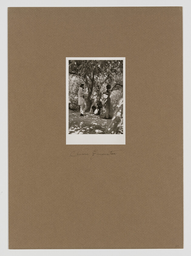 A sepia-toned photo of three people in a garden, two in dresses and one in a suit, surrounded by trees.