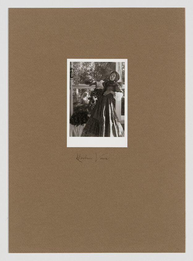 A sepia-toned photograph of a woman in a vintage dress with voluminous sleeves and a full skirt, posing with one hand on her hip and the other holding a bunch of flowers. The photo is mounted on a brown paper with a handwritten signature at the bottom right corner.