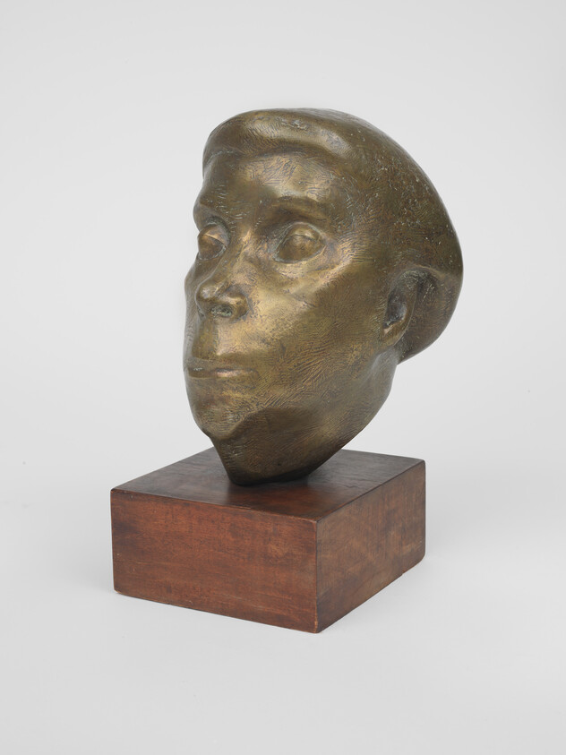 Bronze sculpted human head with stylized features mounted on a wooden block base.