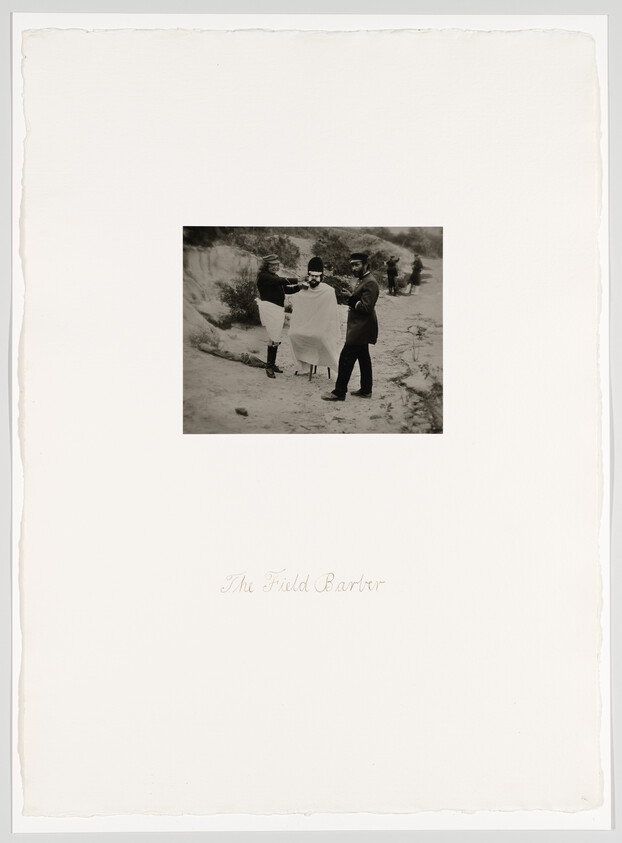 A field barber gives a soldier a shave outdoors while two men assist nearby.