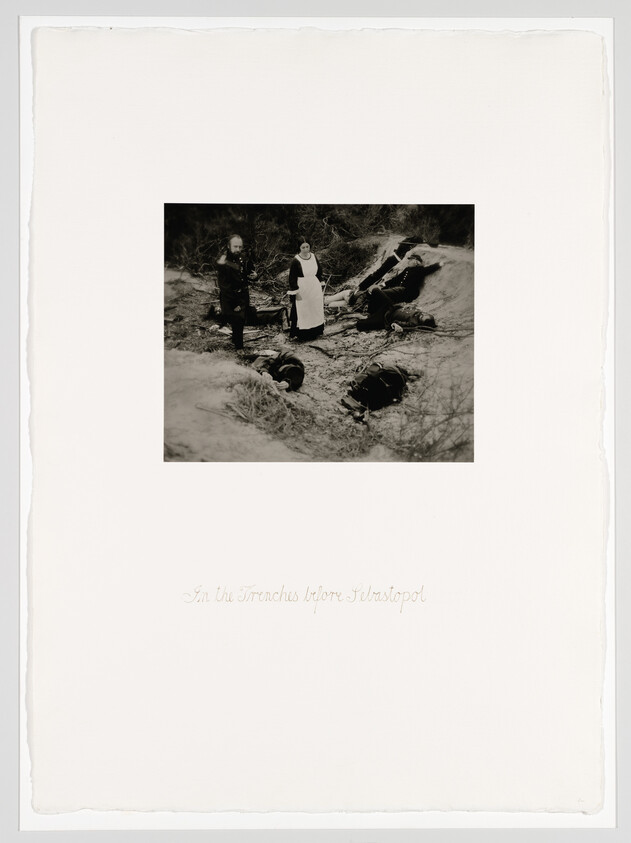 A nurse and two men stand in a muddy trench beside wounded soldiers.