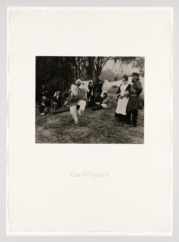 A man in costume dances in front of seated soldiers and standing nurses by a riverside.