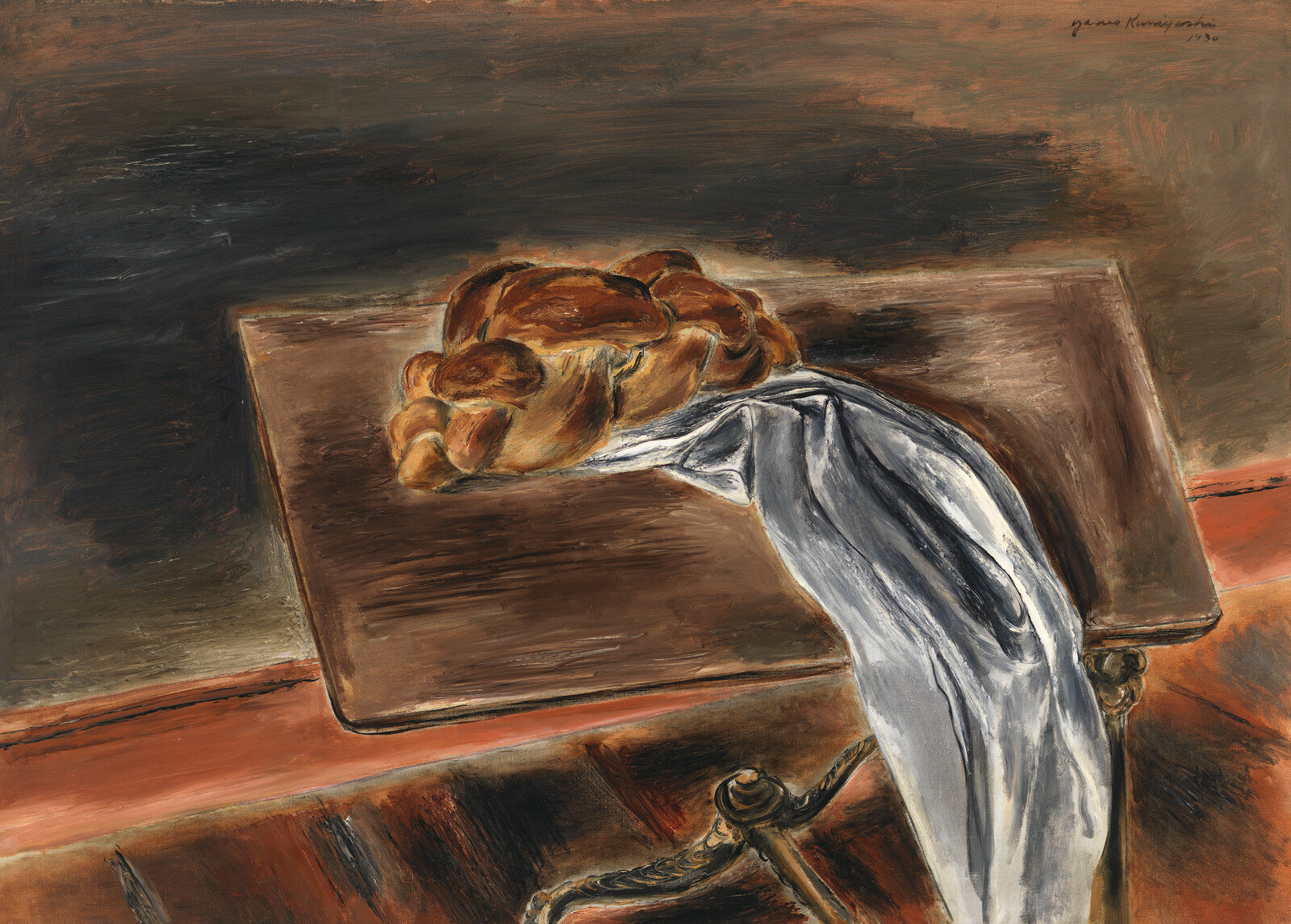A braided loaf of bread rests on a wooden table with a white cloth draped over the edge.
