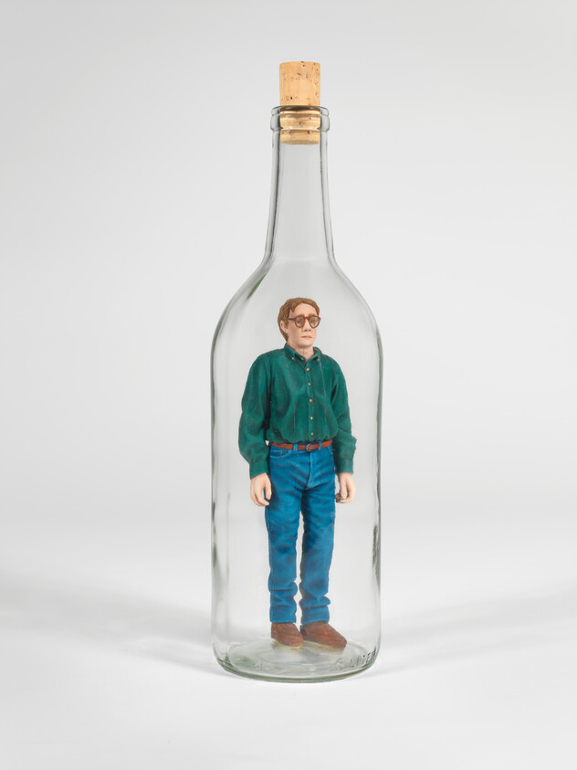 A miniature figure of a man standing inside a clear glass bottle sealed with a cork.