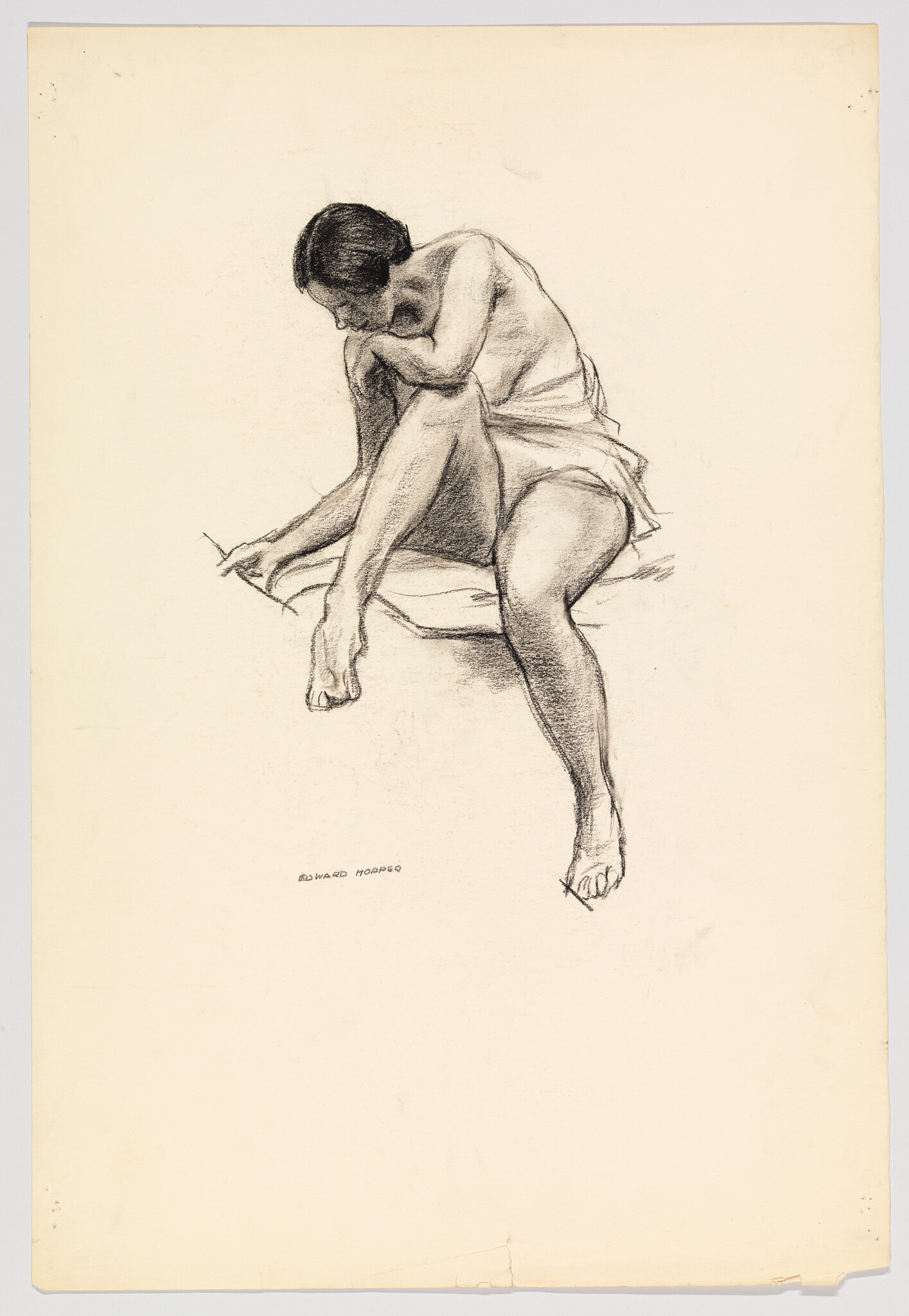 A seated woman in a short dress bends forward, touching her foot while looking down.