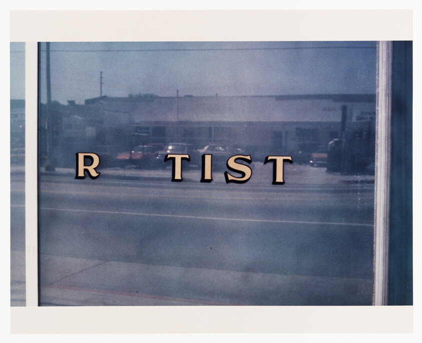 Storefront window with gold letters reading "R TIST" reflected street visible behind glass.