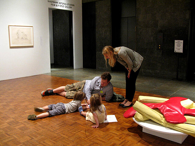 Two children and two adults gathered on the floor of a gallery drawing.