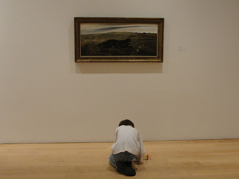A child works on the gallery floor in front of a painting.