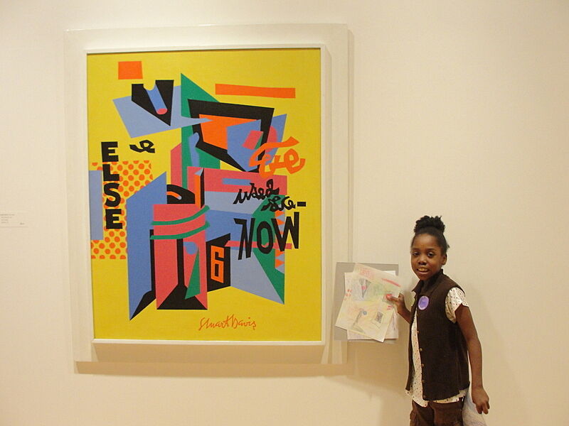 A girl holds up her interpretive drawing next to the artwork.