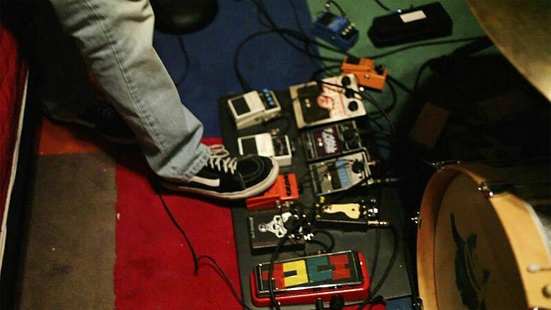 Someone's leg and shoe stepping on one of many guitar pedals in view.