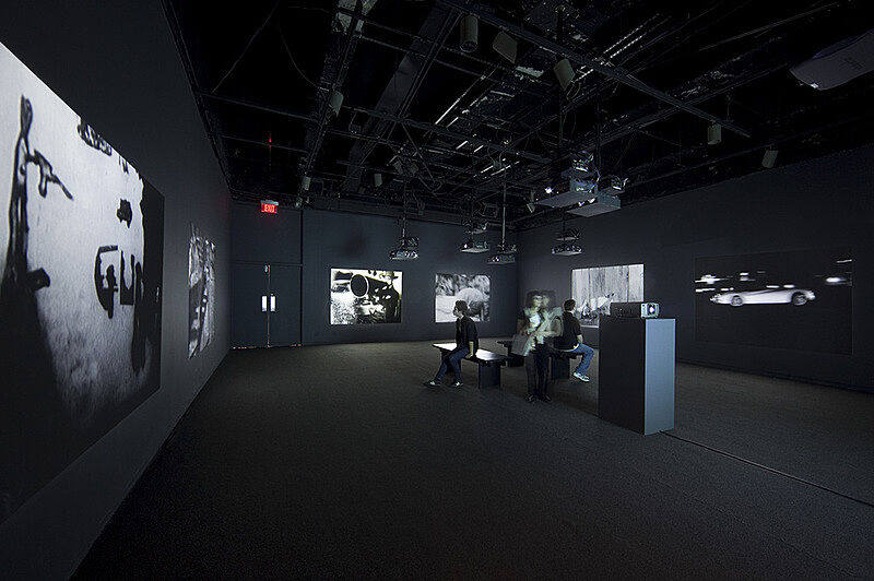 A darkened gallery with people sitting on benches.