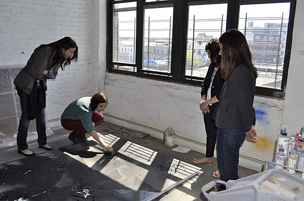 Artist drawing on the ground while members look on.
