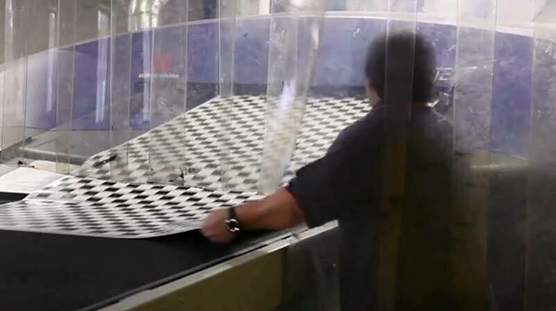 A worker pulls a large section of vinyl out of a machine.