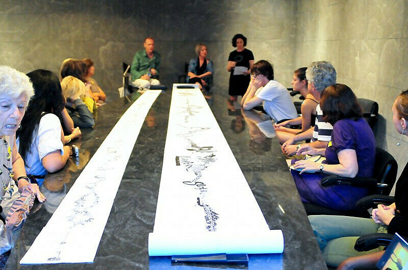 A group gathers around a long scroll as the artists talk about their work.