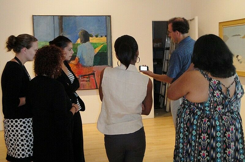 A group of people gather around a smartphone in a gallery.
